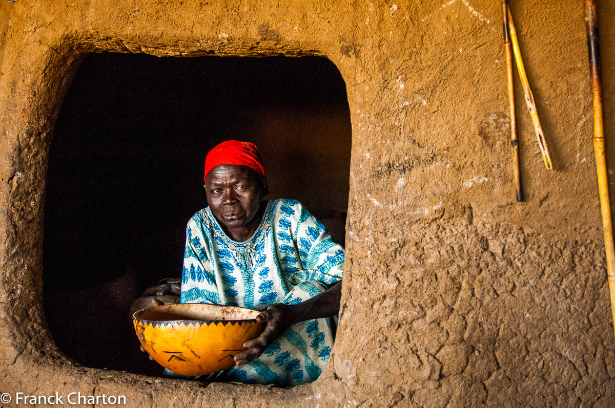 Femme Nuba présentant une calebasse de bière de sorgho, devant sa hutte. 