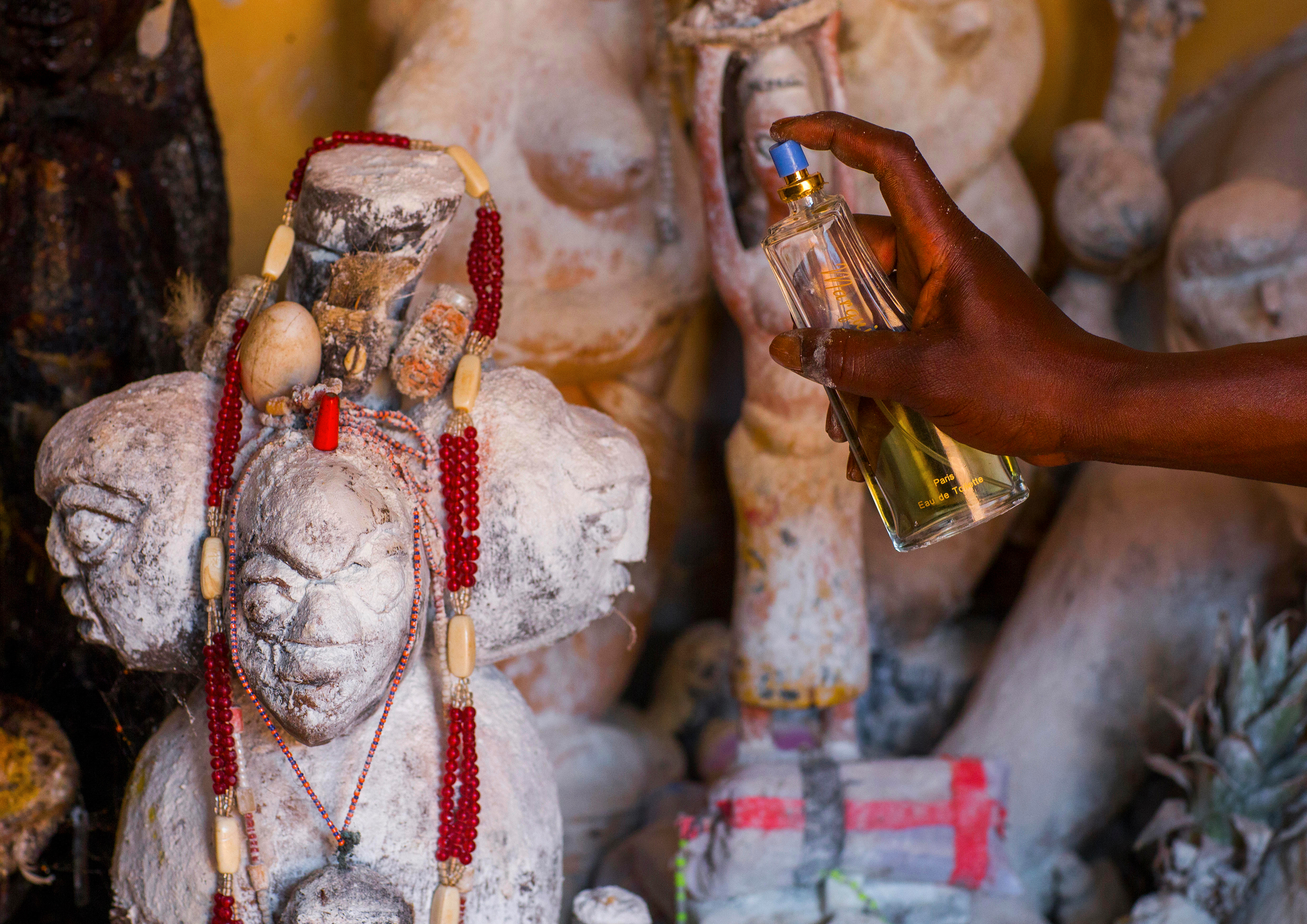Prêtre vaudou parfumant les statues sacrées au cours d'une cérémonie au Bénin