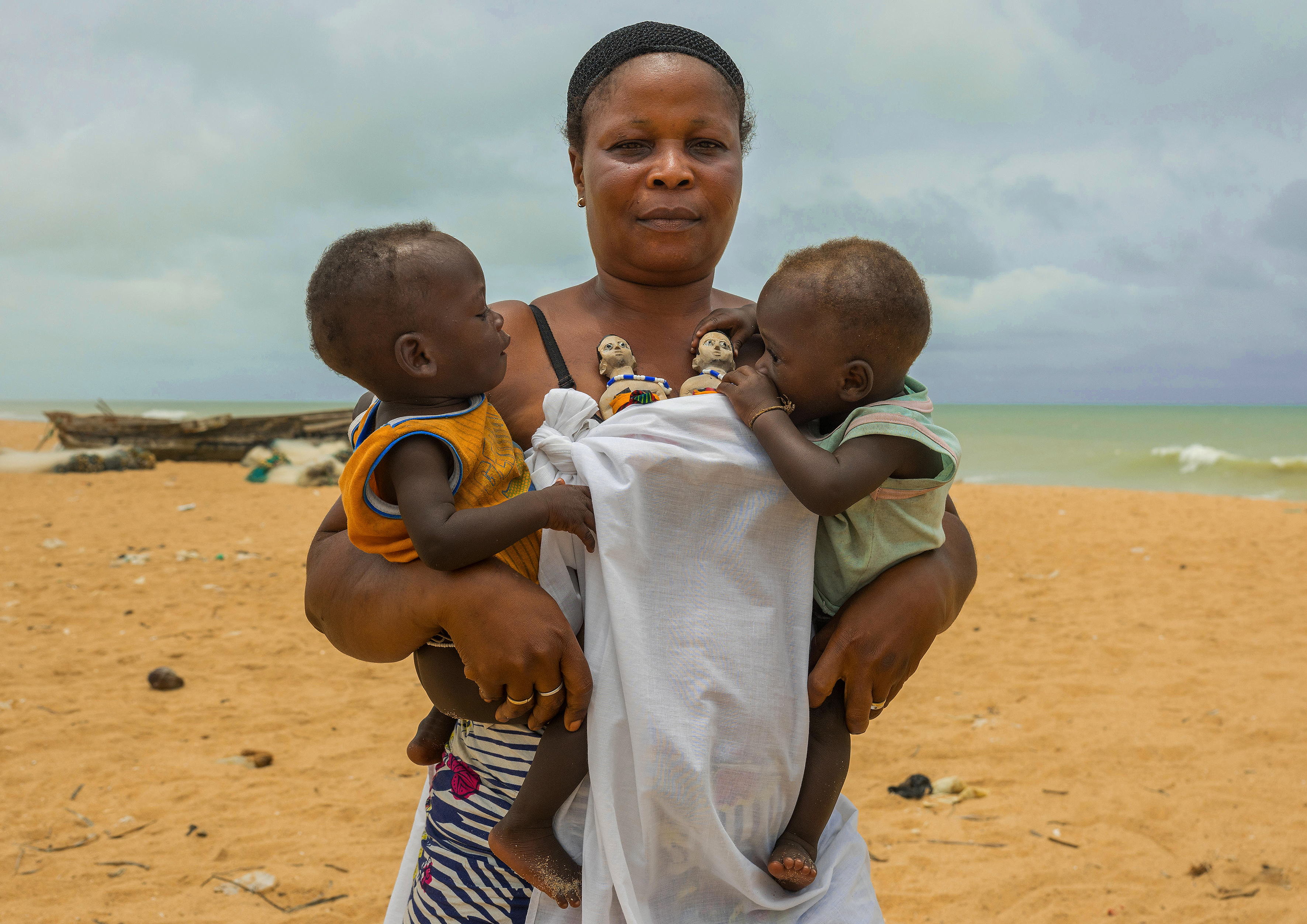 À Ouidah, une mère porte au corsage les statuettes de ses jumeaux morts et dans les bras ses derniers jumeaux 