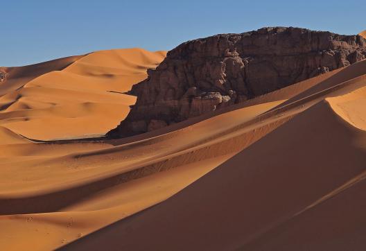Trek au détour d'un rocher au milieu de dunes dans la Tadrart
