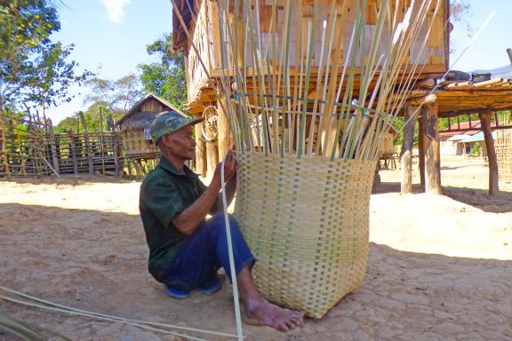 Trekking vers un homme confectionnant un grand panier dans un village du sud du Laos