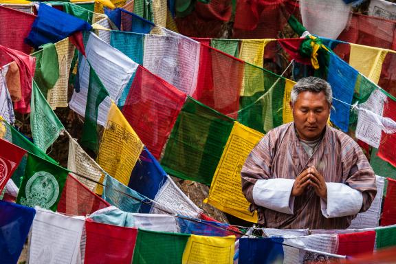 Bhoutanais en prière entouré de drapeaux à prières au Bhoutan