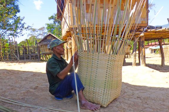 Trekking vers un homme confectionnant un grand panier dans un village du sud du Laos