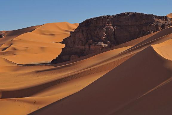 Trek au détour d'un rocher au milieu de dunes dans la Tadrart