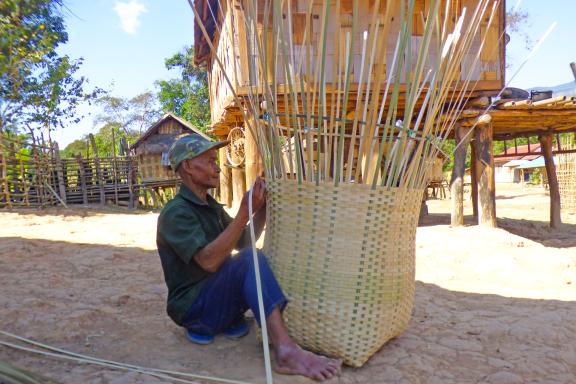 Trekking vers un homme confectionnant un grand panier dans un village du sud du Laos
